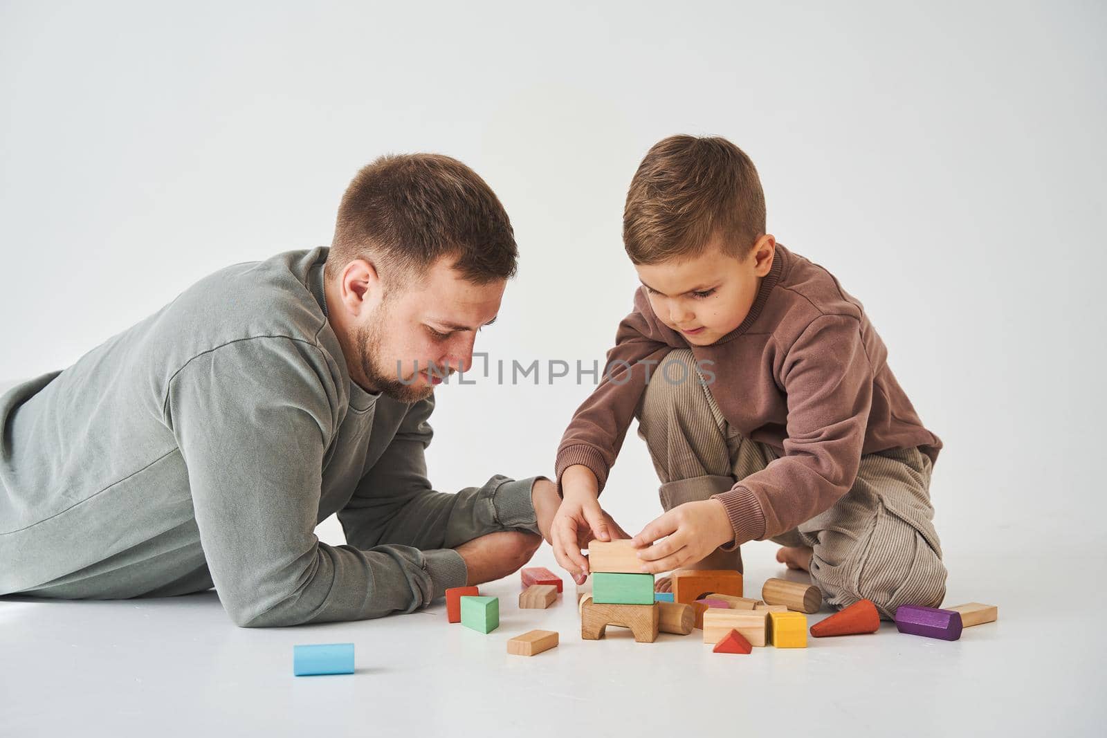 Paternity. Son and dad playing with colored bricks toy on white background. Father takes care of his kid. by Rabizo