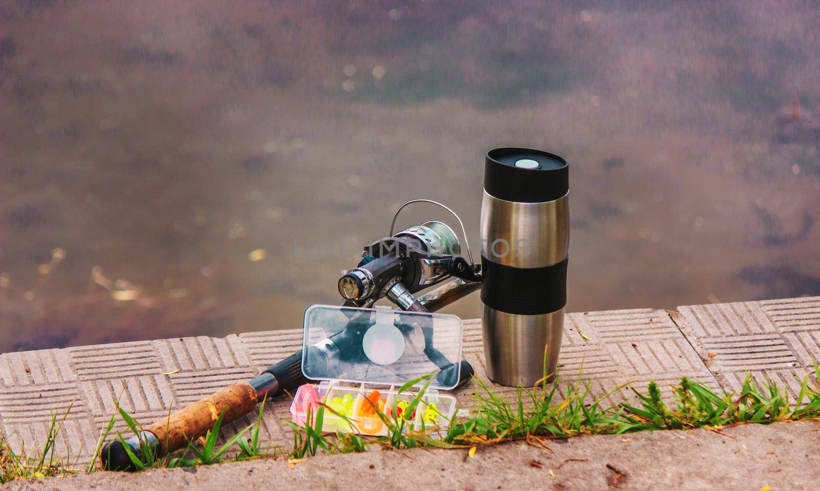 Fishing rod, spinning reel and a cup of hot coffee on the bank of the river pier. Out-of-town vacation concept. Nature. Selective focus