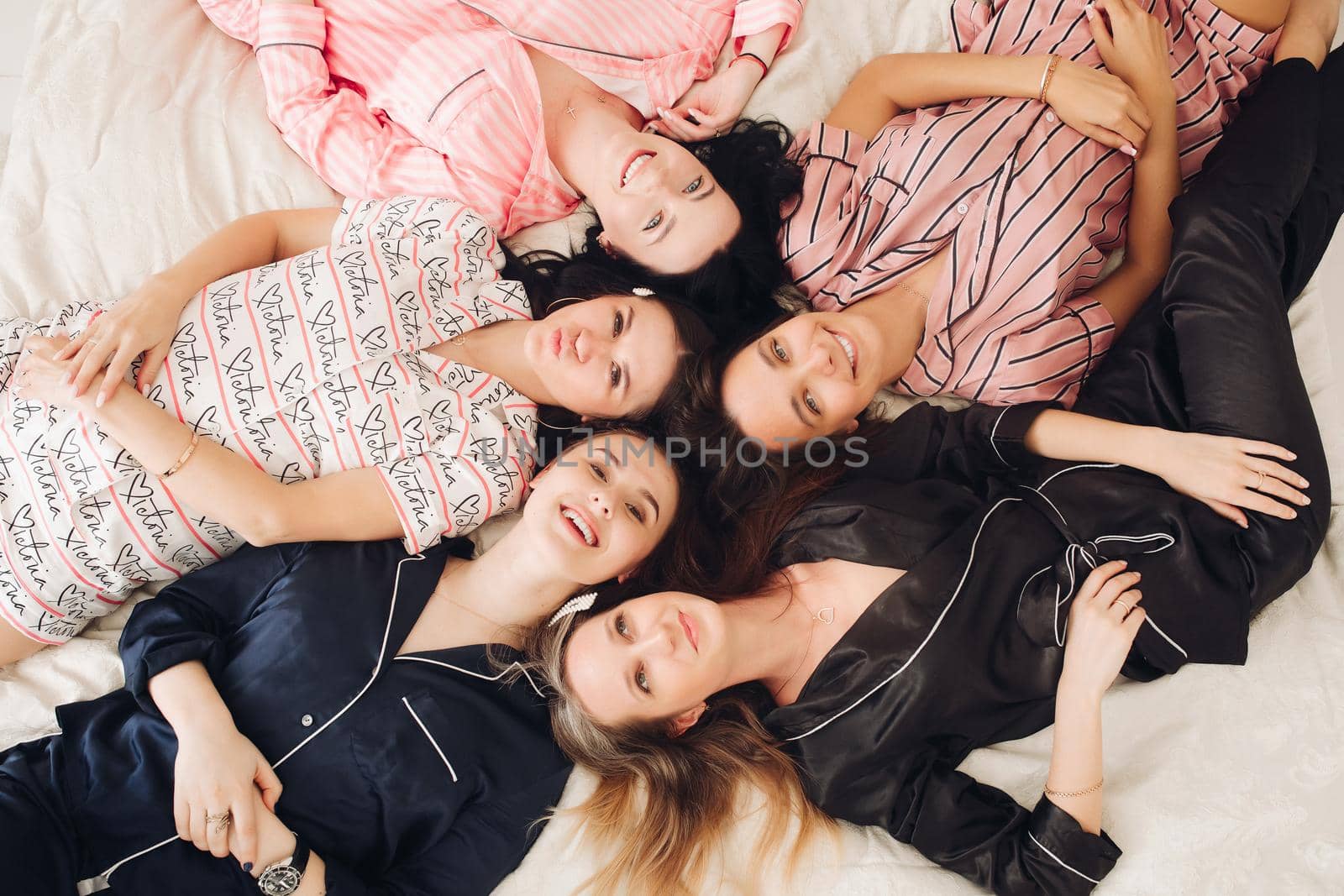 Top view relaxing young girl friends lying on bed having fun posing together medium shot. Group of happy female enjoying pajamas party have positive emotion celebrating holiday