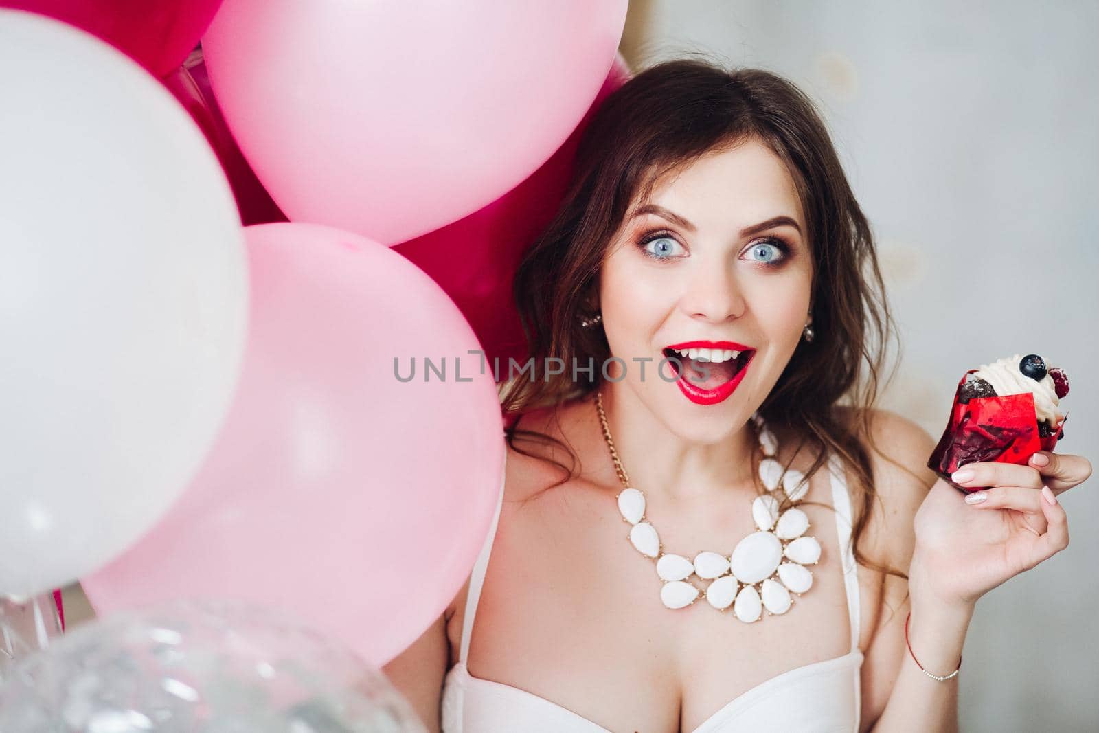 Portrait of pretty surprised brunette bride-to-be with berry cupcake and pink air balloons.
