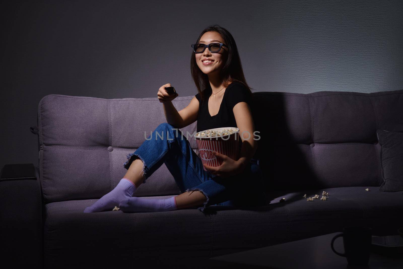 Beautiful young Asian woman watching TV at home. Eating popcorn. Time at home, isolation