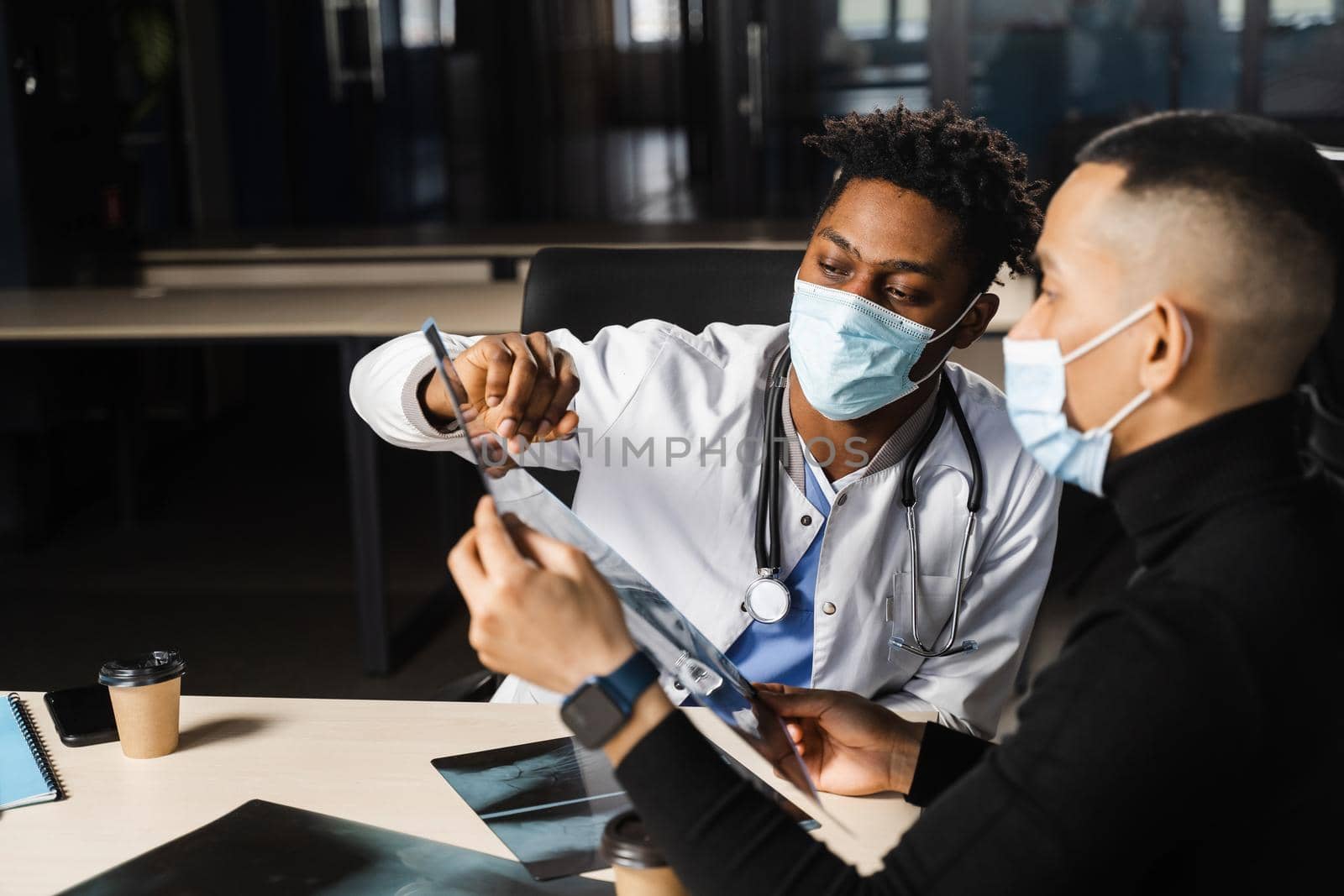 African doctor show x-ray asian patient. Pneumonia and pleurisy. Black surgeon analyzing x ray and diagnosis patient in medical clinic. by Rabizo