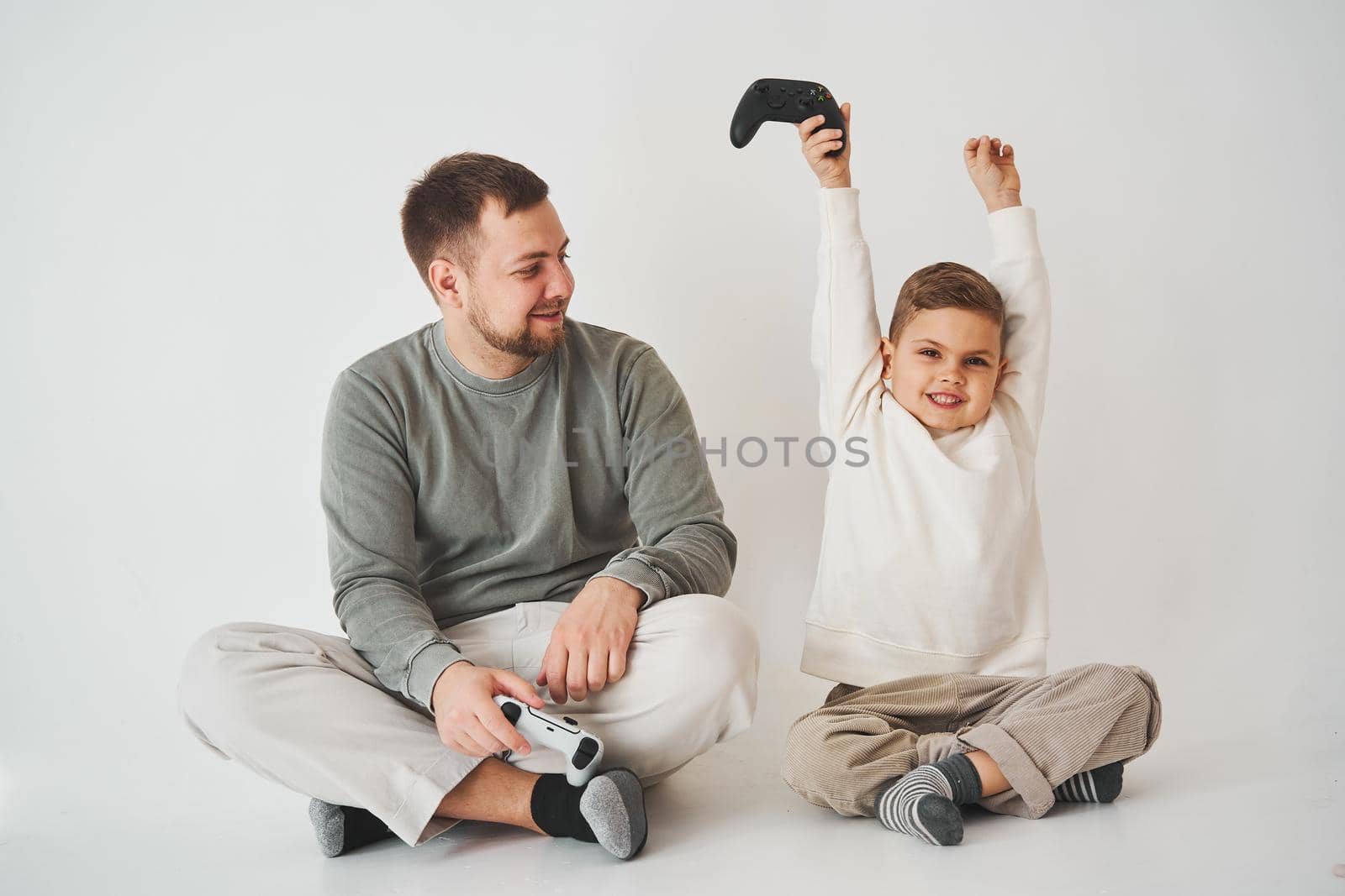 Son won father in game on console. Happy child with gamepad raises his hands up and rejoices in the victory in the game
