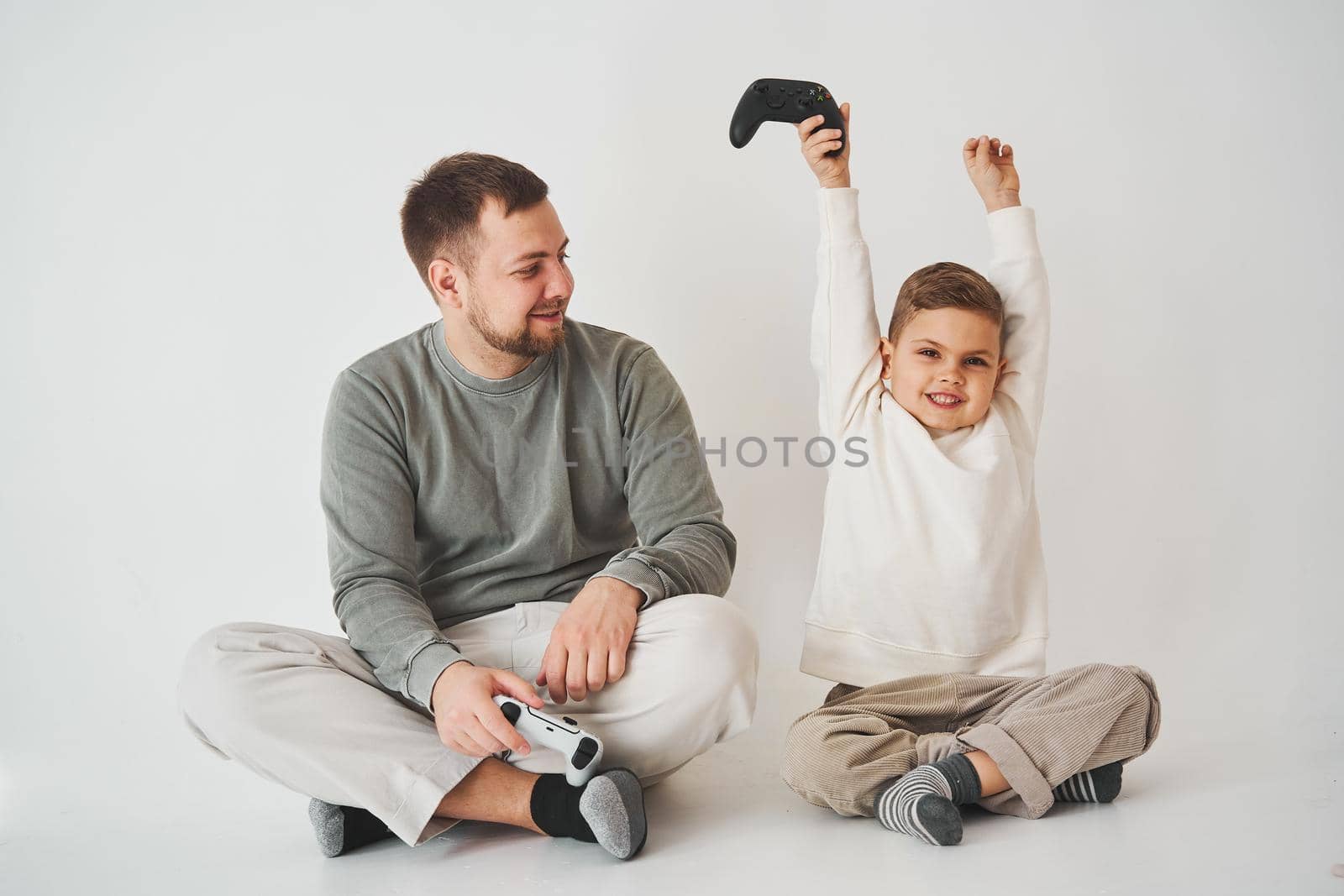 Son won father in game on console. Happy child with gamepad raises his hands up and rejoices in the victory in the game. by Rabizo