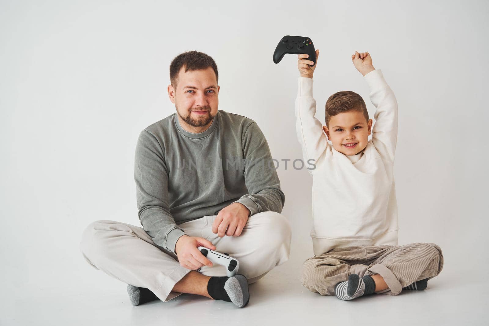 Son won father in game on console. Happy child with gamepad raises his hands up and rejoices in the victory in the game