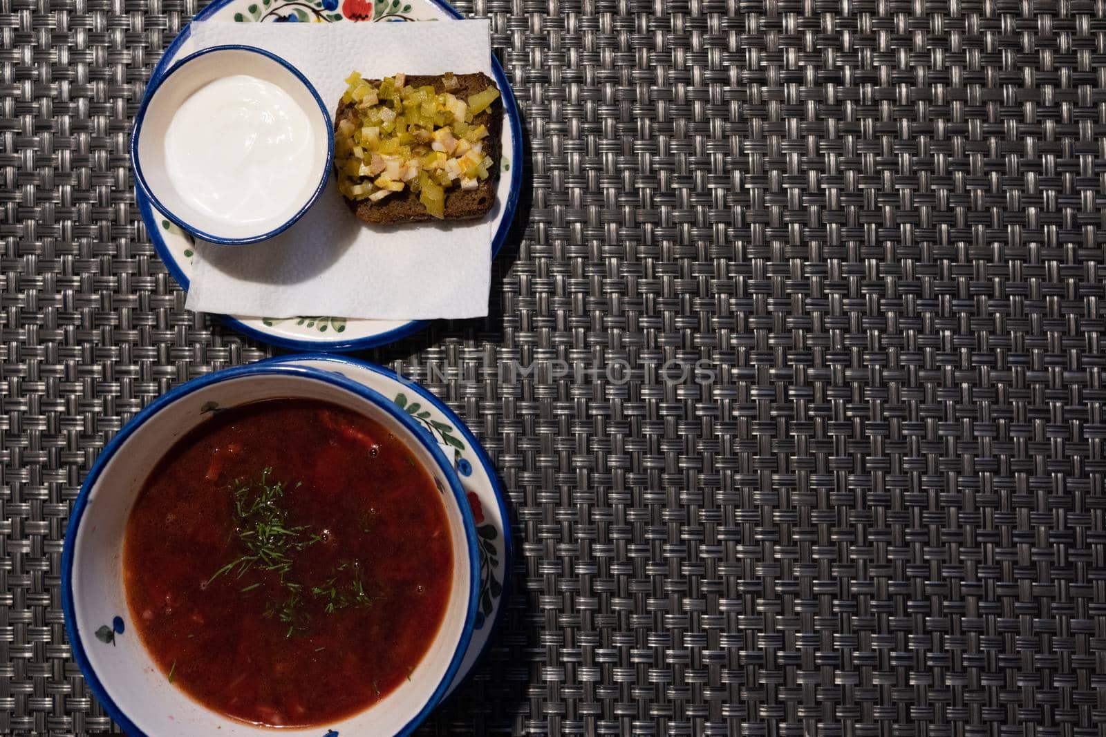 Borscht in a plate is decorated with greens. a cup with sour cream and a sandwich with pickles and bacon for borscht. Plates with napkins decorated with ornaments in a Russian cuisine restaurant.....