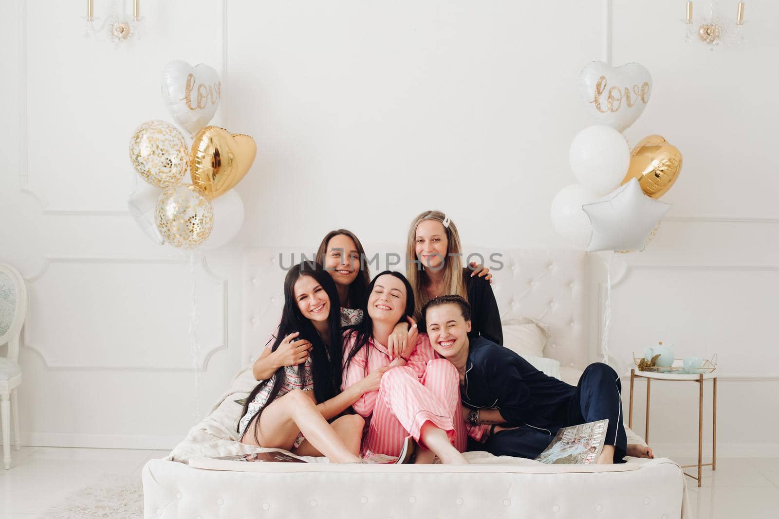 Group of happy girl friends laughing posing on bed enjoying pajamas party by StudioLucky