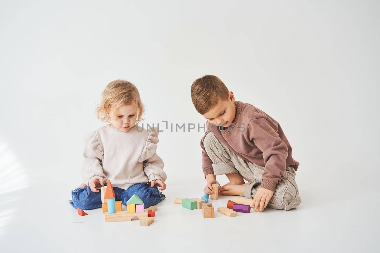 Child girl plays with cheerful kid with toy wooden cubes on white background. Children have smiling and have fun together