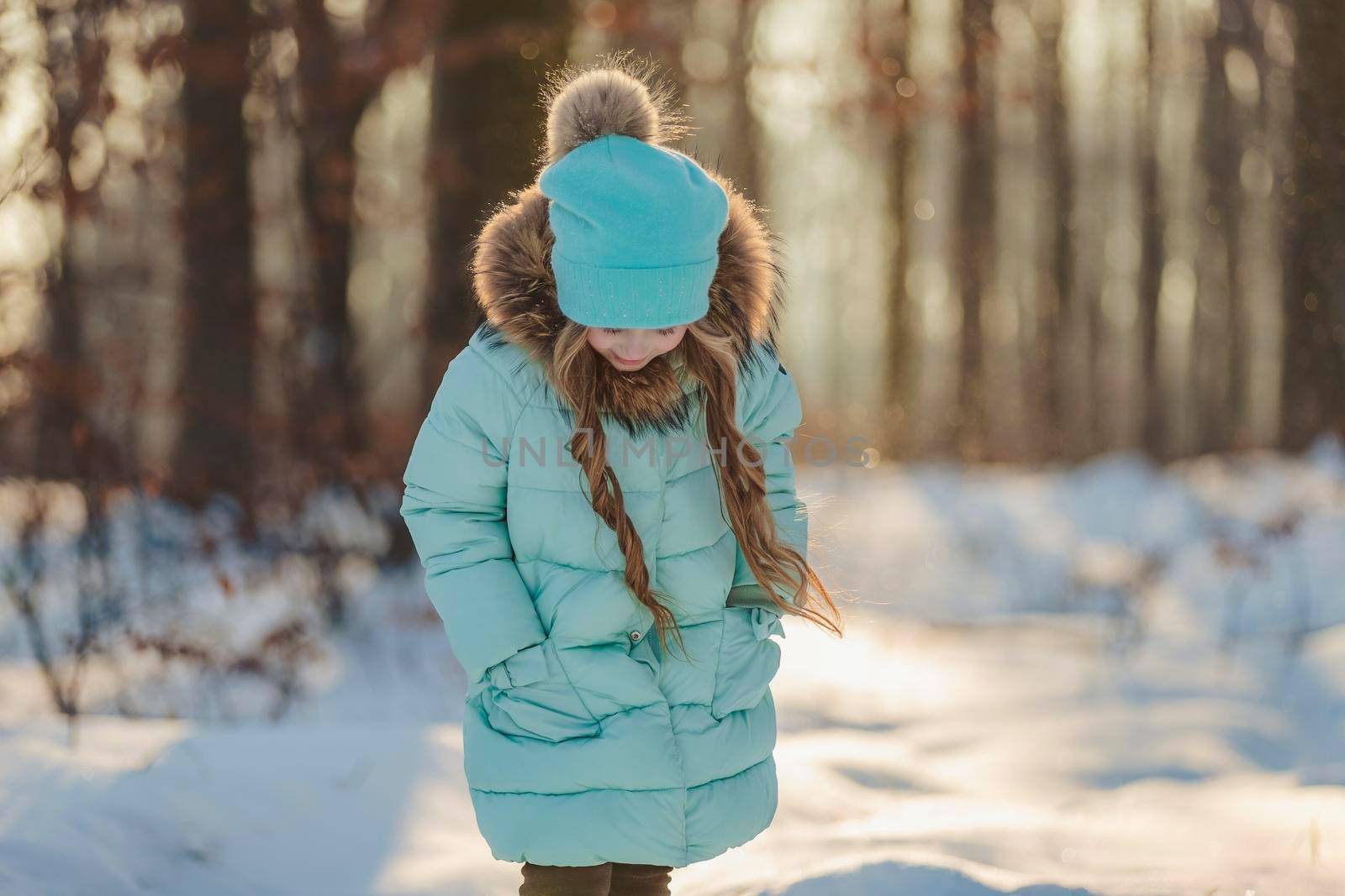 girl in a jacket and hat of turquoise color against the backdrop of a snowy forest