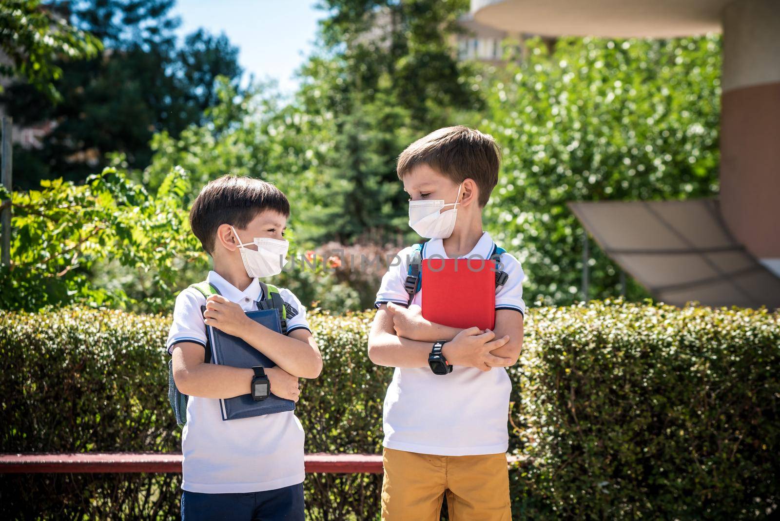 two boys, schoolchildren in black school uniforms with backpacks in a medical mask go to school independently, hold hands, friendship concept, study concept during coronavirus, back to school.