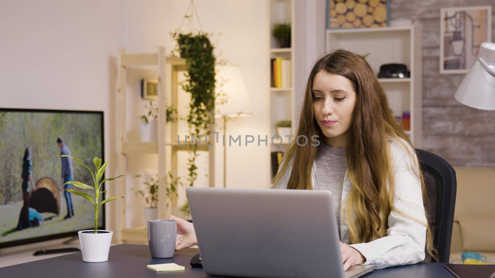 Girl working on laptop from home office. Girl taking a sip of coffee.