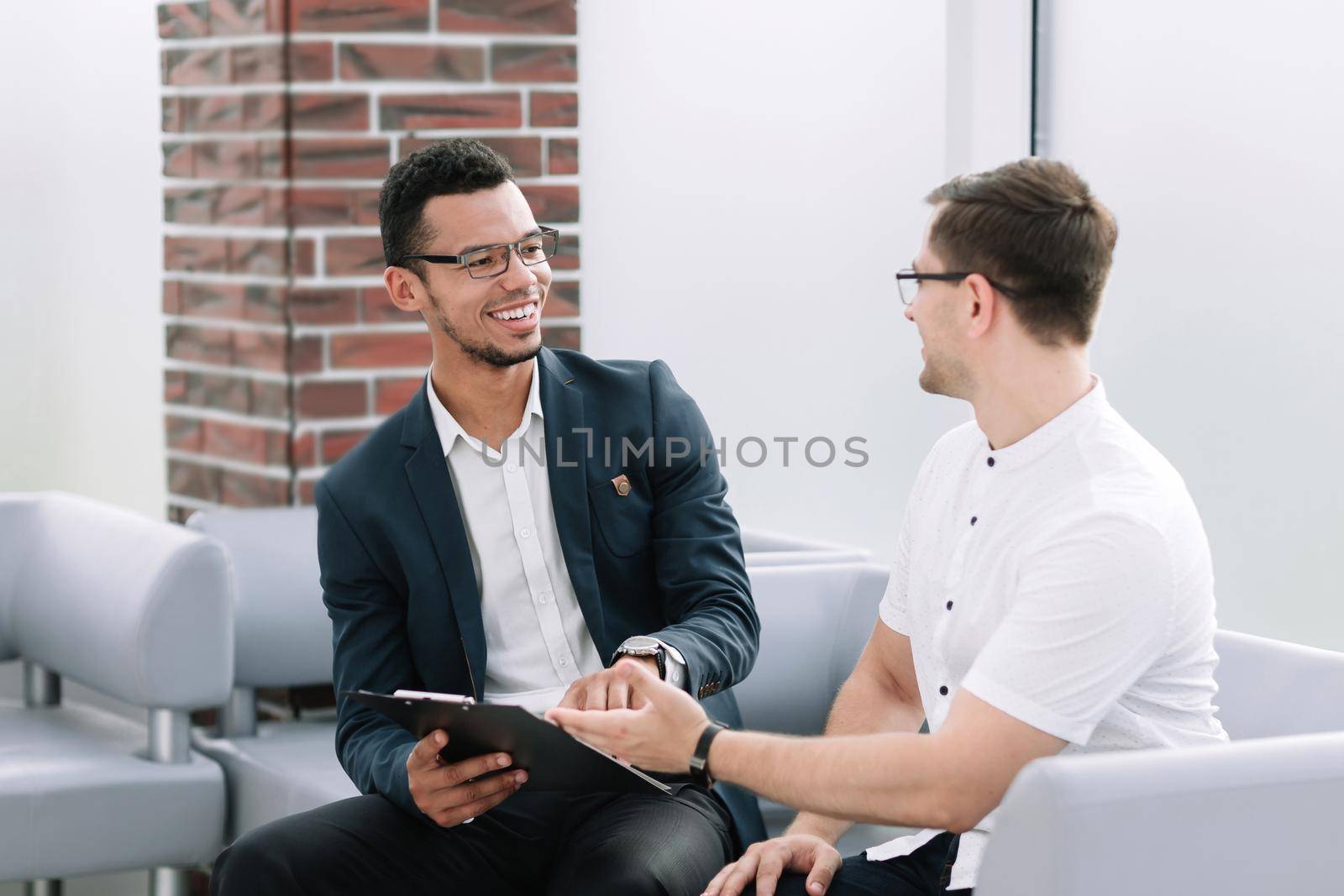 business colleagues discussing business document sitting in office lobby. by SmartPhotoLab