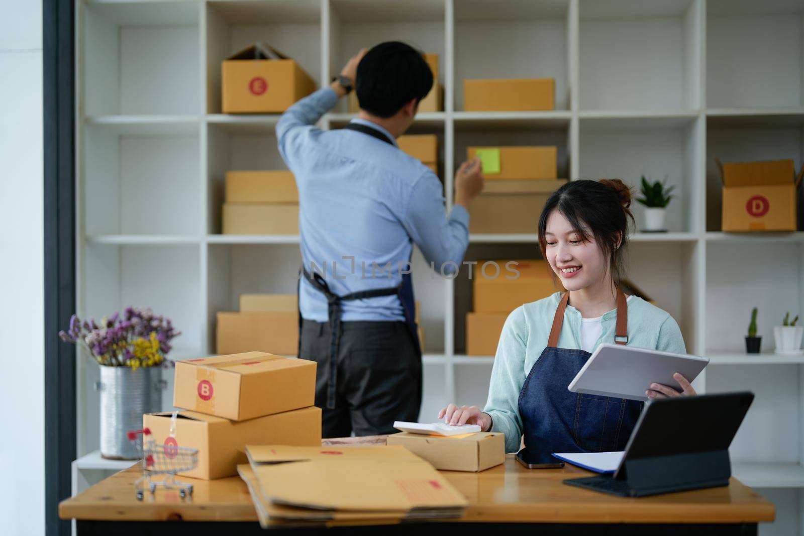 startup small business owner working with tablet at workplace. freelance man and woman seller check product order, packing goods for delivery to customer. Online selling, e-commerce, shipping concept by nateemee