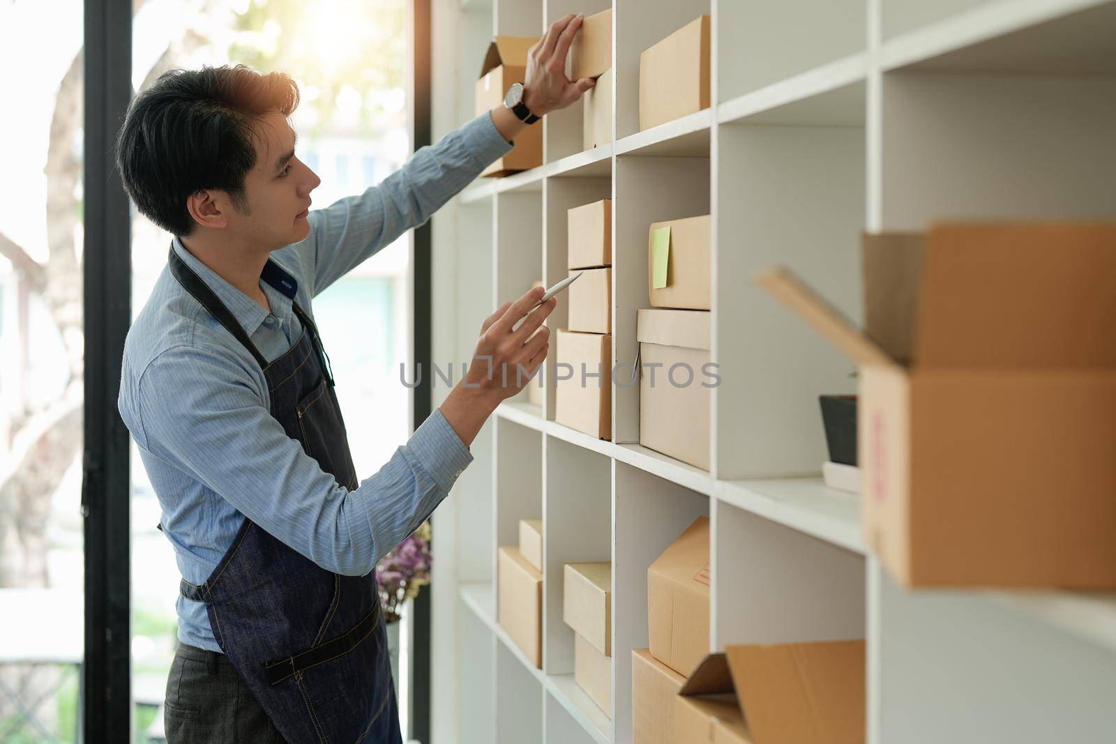 Young attractive asian owner startup business look at camera work happy with box at home prepare parcel delivery in sme supply chain, procurement, omnichannel or coronavirus quarantine concept.
