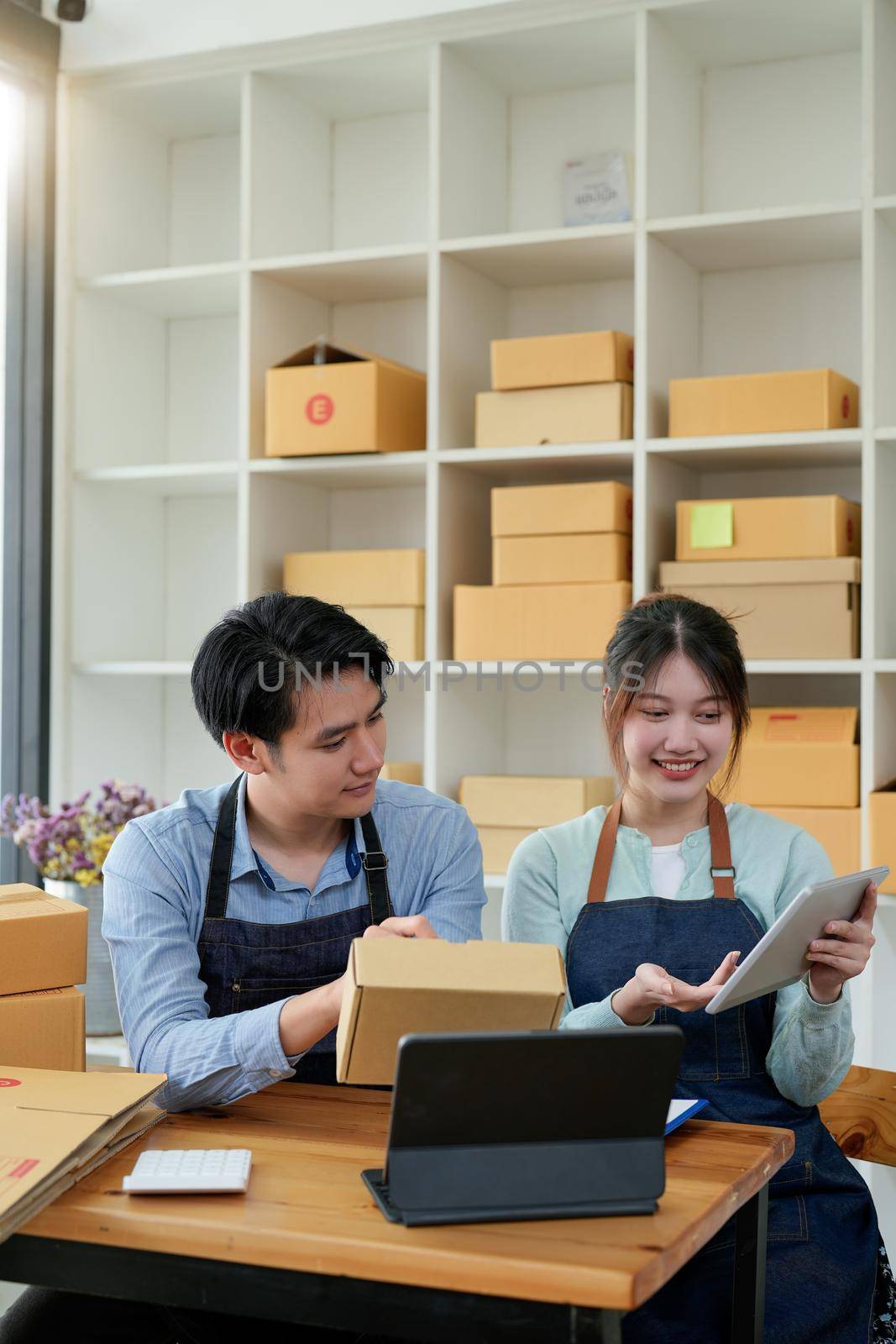 startup small business owner working with tablet at workplace. freelance man and woman seller check product order, packing goods for delivery to customer. Online selling, e-commerce, shipping concept by nateemee