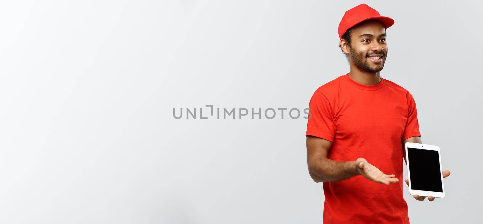 Delivery Concept - Portrait of Handsome African American delivery man or courier showing tablet on you to check the order. Isolated on Grey studio Background. Copy Space. by Benzoix