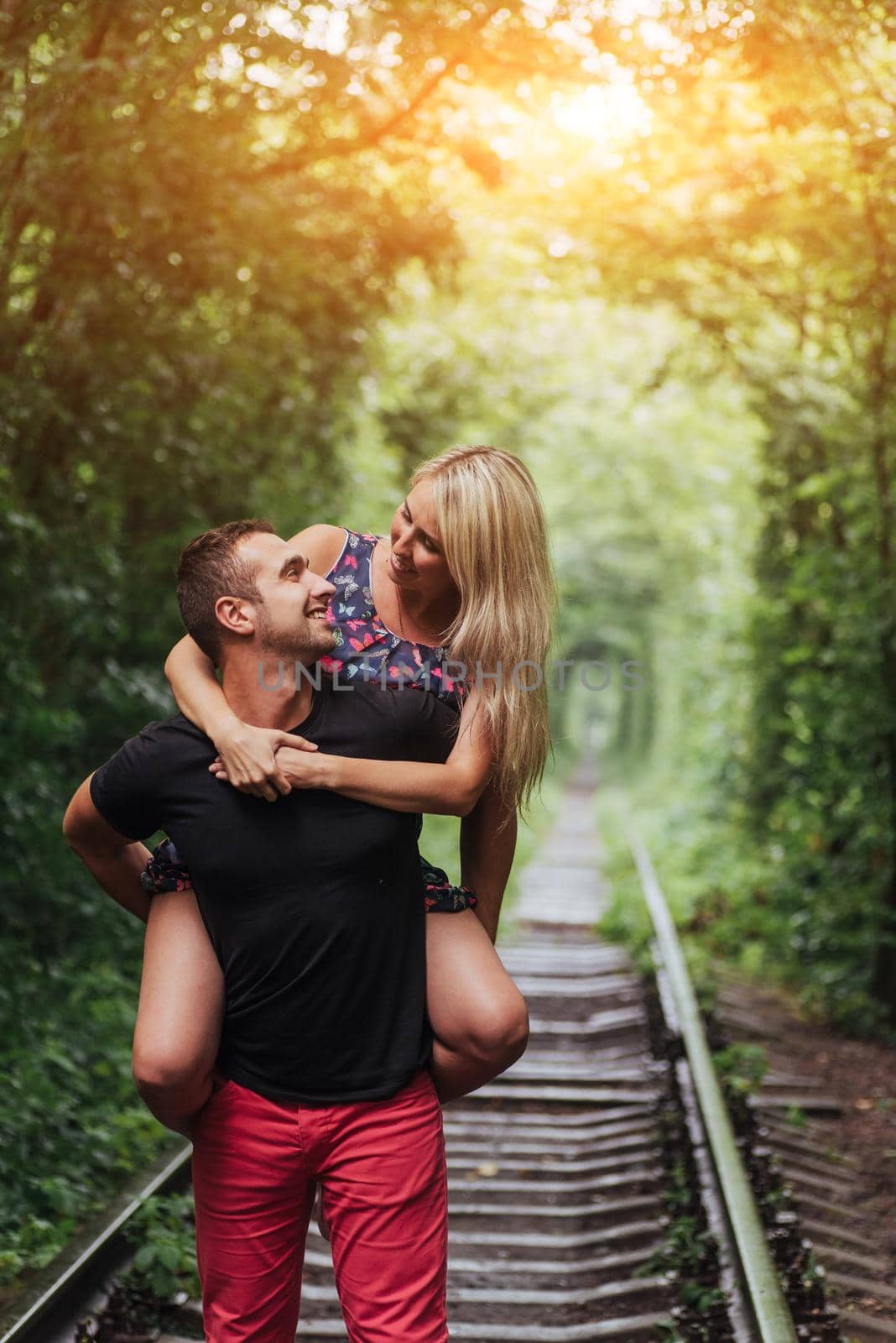 Loving couple in a tunnel of green trees on railroad.