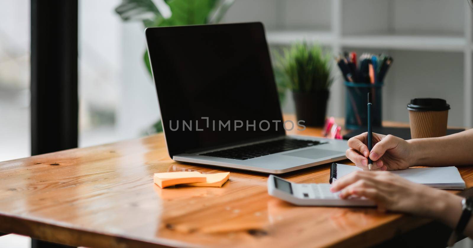 Close up of businessman or accountant hand holding pen working on calculator and laptop computer to calculate business data during make note at notepad, accountancy document at office