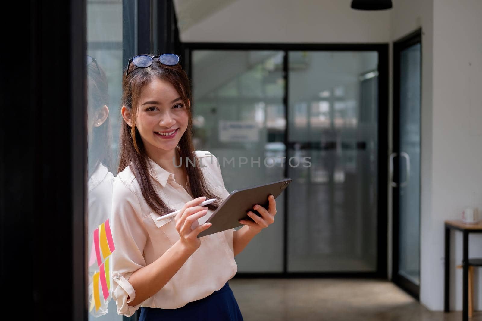 Portrait woman manager holding digital tablet and standing in modern office. Asian female using stylus with tablet.