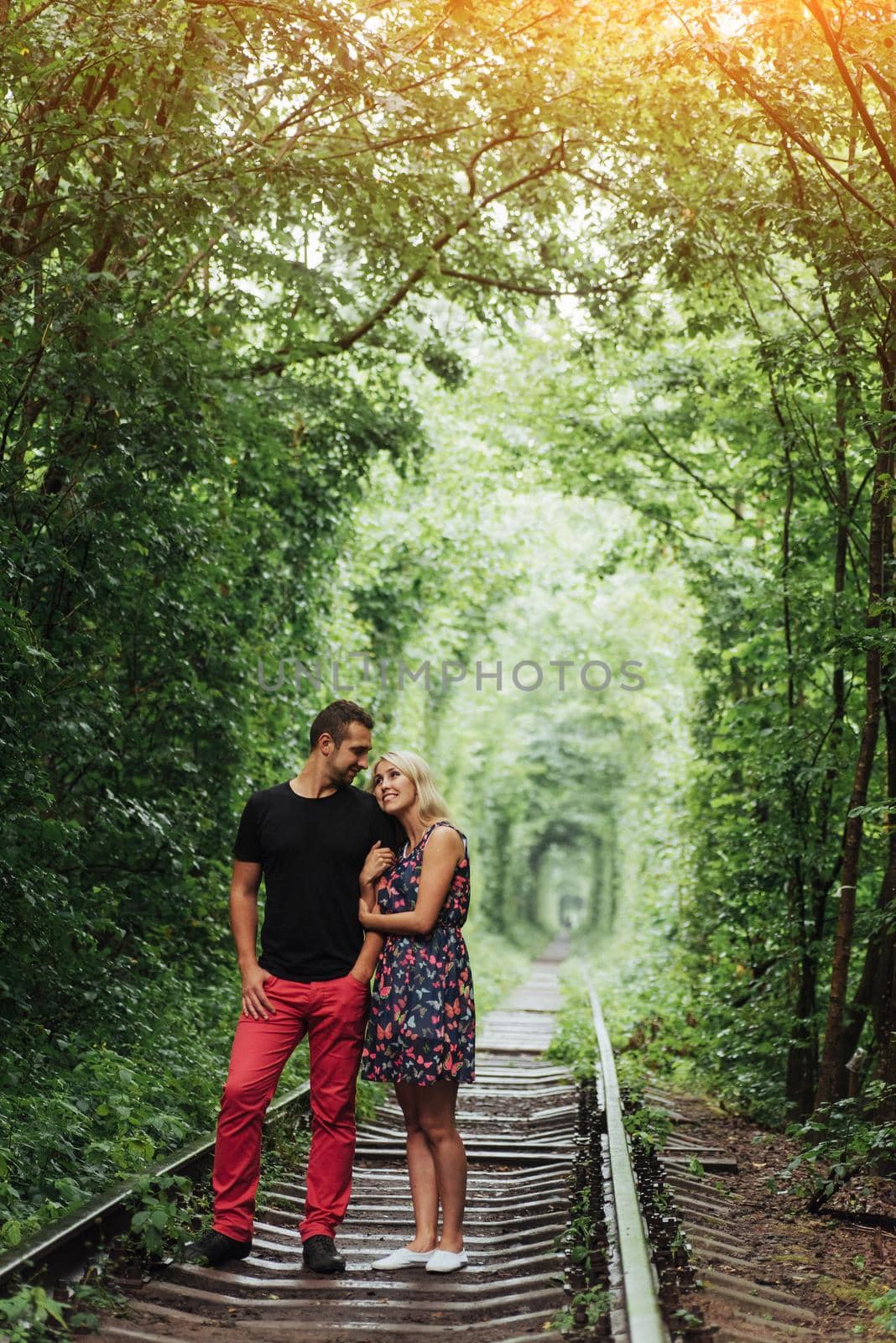 Loving couple in a tunnel of green trees on railroad by Standret