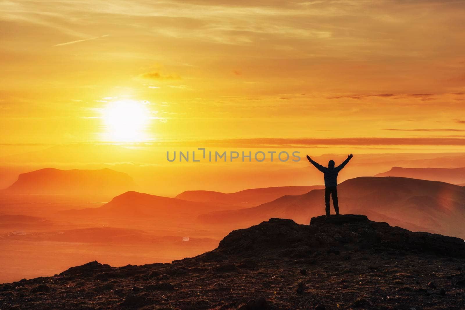 Happy man standing on a cliff at sunset.