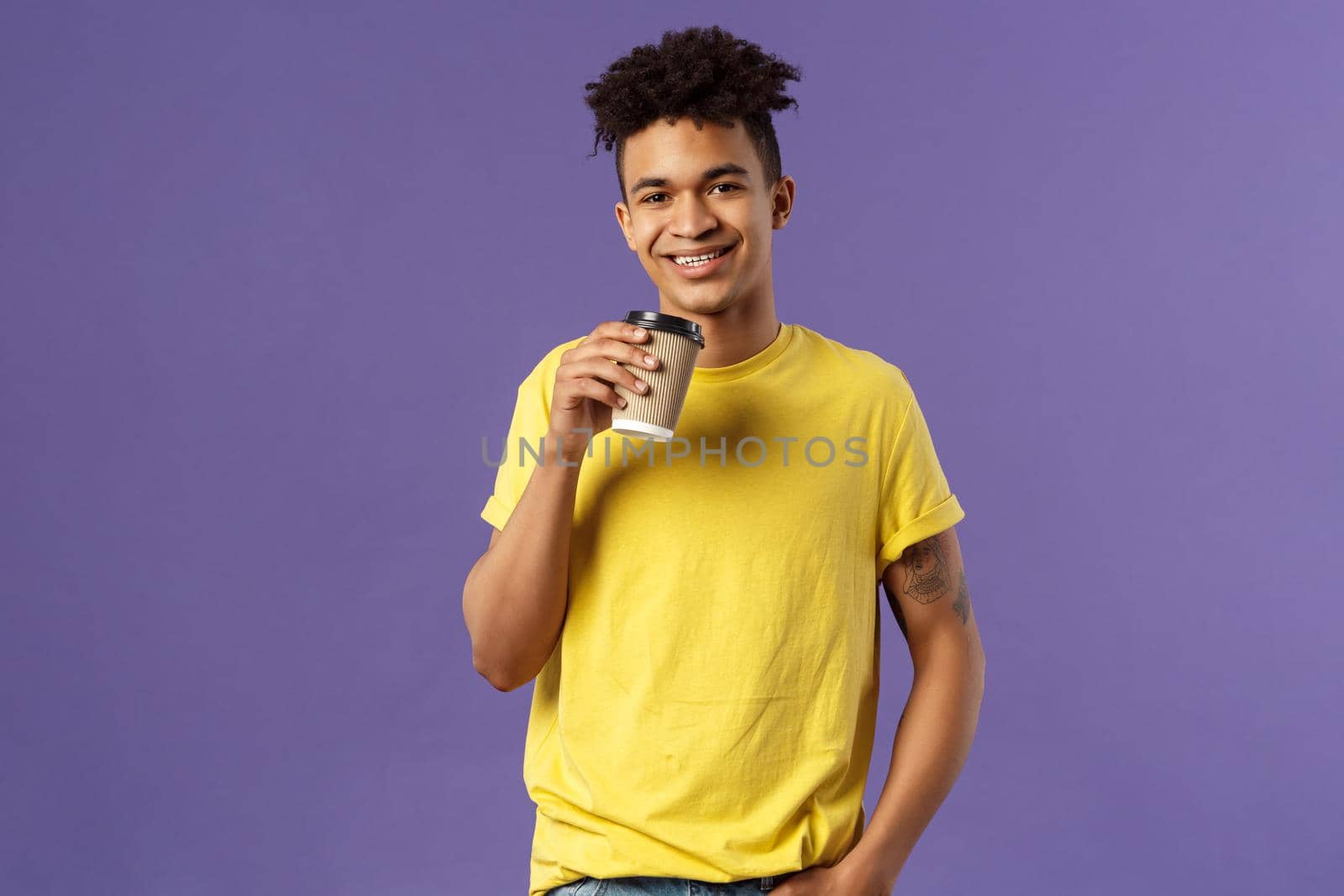Portrait of good-looking young male student with dreads, tattoos, casually drinking coffee from take-away cup, visit favorite cafe, smiling cheerful, enjoying perfect warm sunny day.