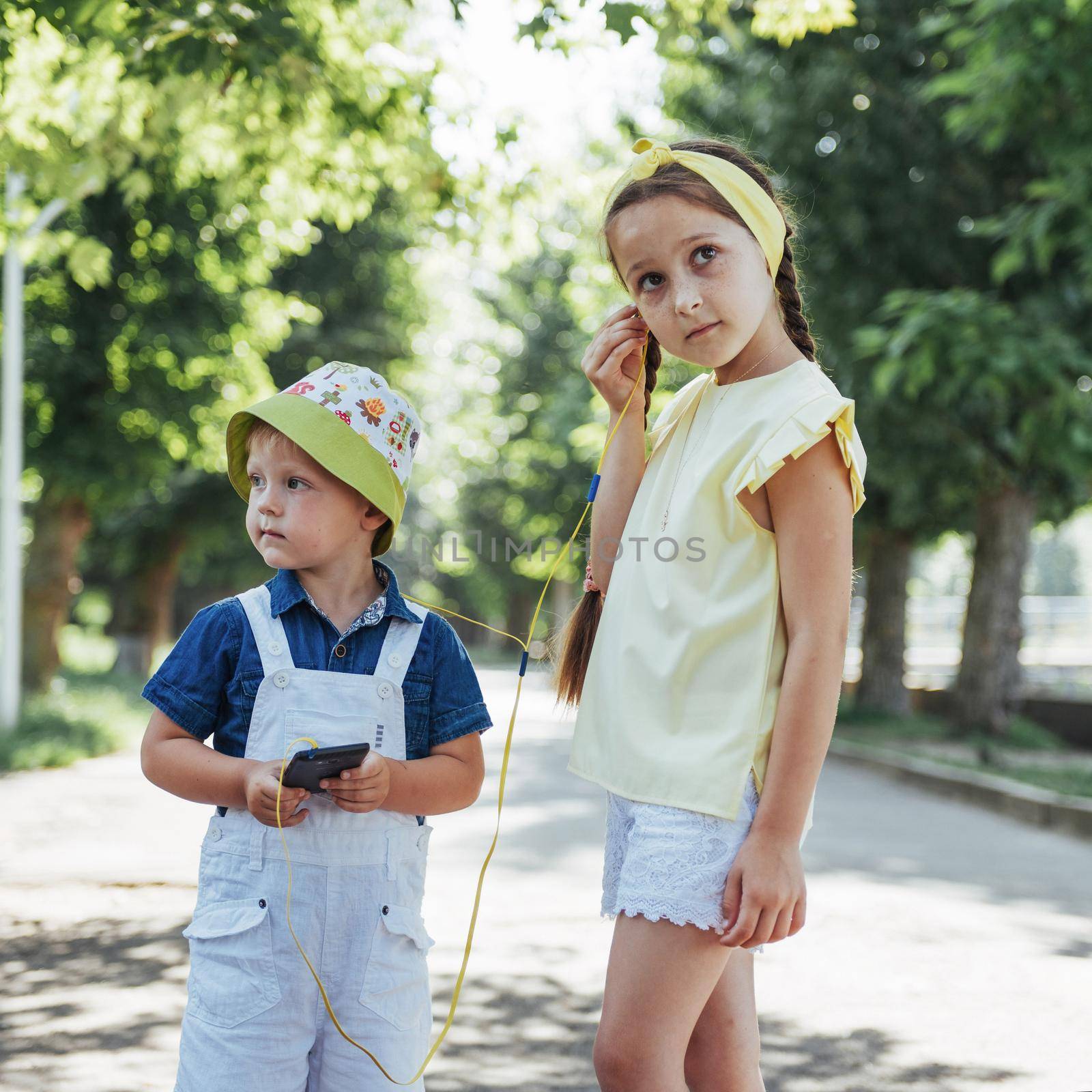 Cute girl and boy listening to music through headphones on the street.