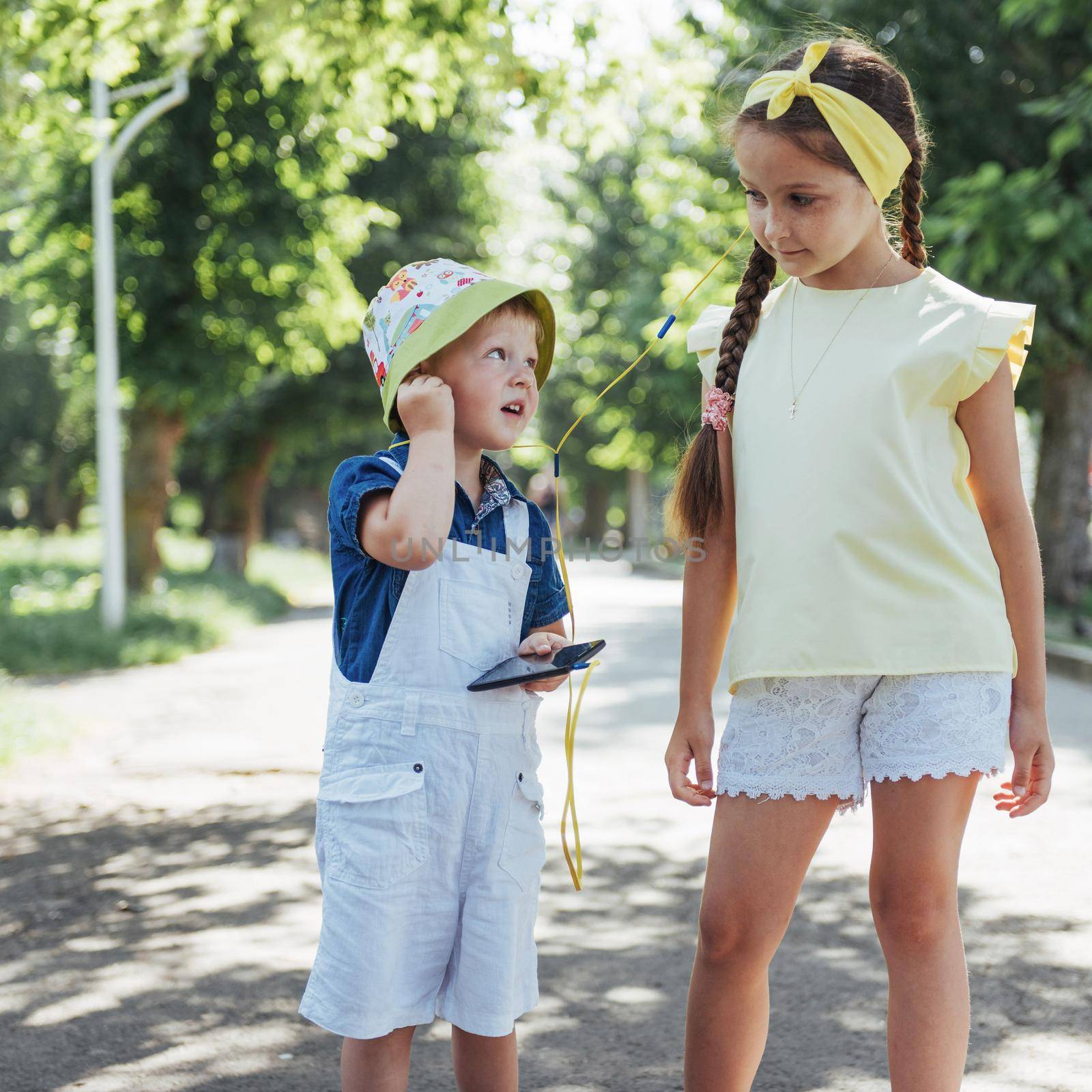 Cute girl and boy listening to music through headphones on the street.