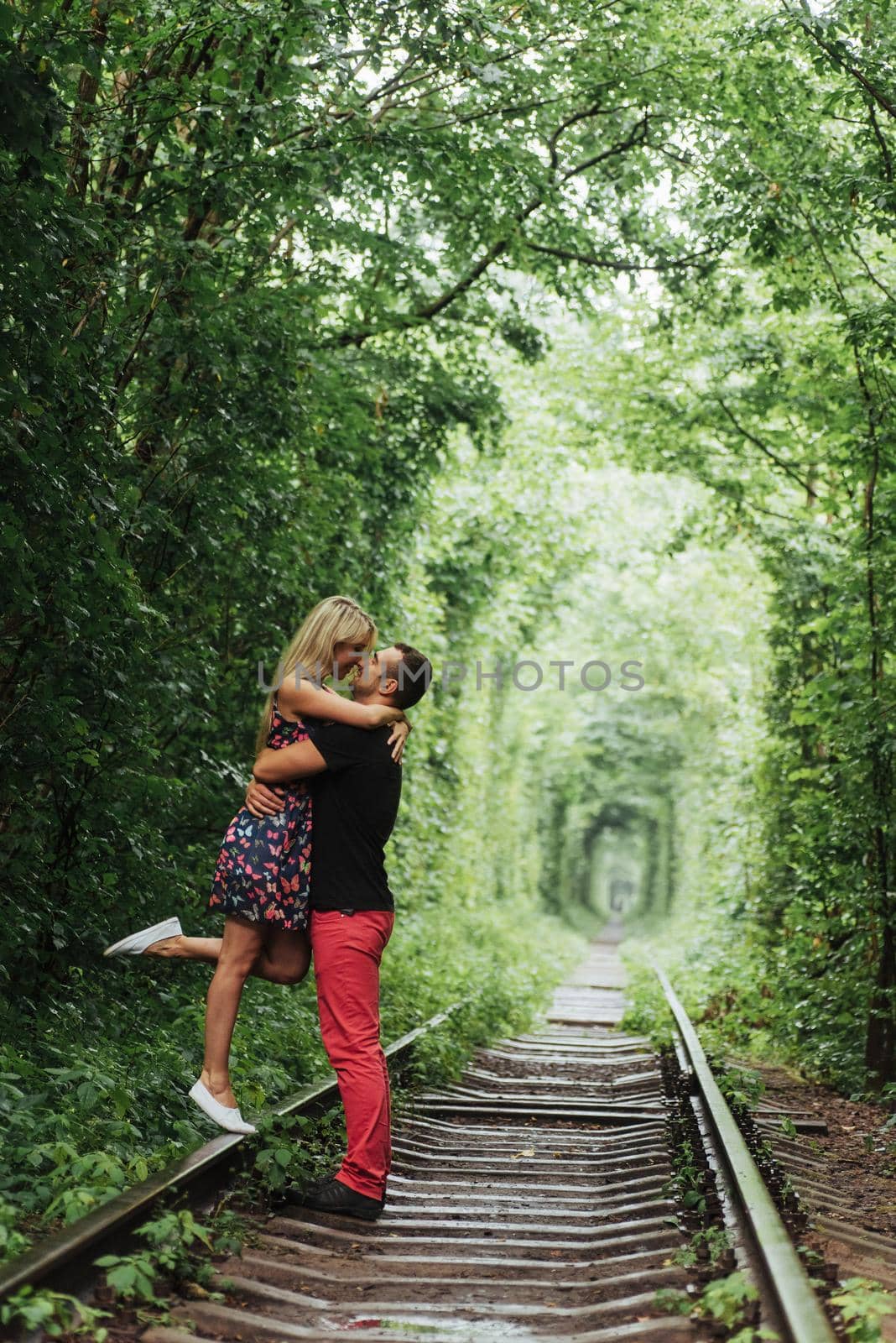 Loving couple in a tunnel of green trees on railroad.