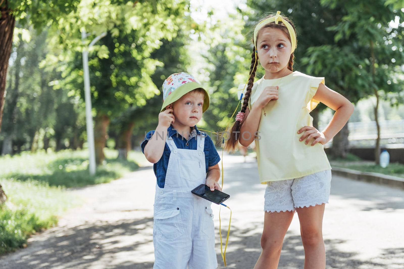 Cute girl and boy listening to music through headphones on the street.