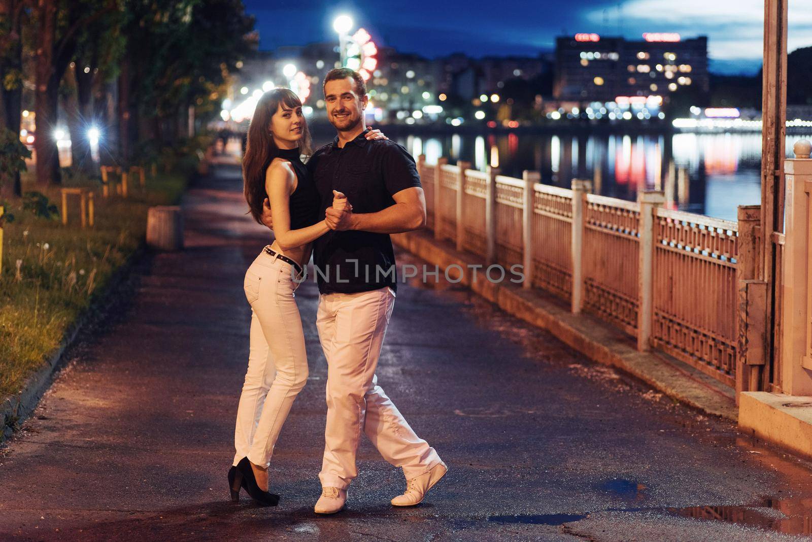 young couple dancing tango on the embankment of the river in the evening