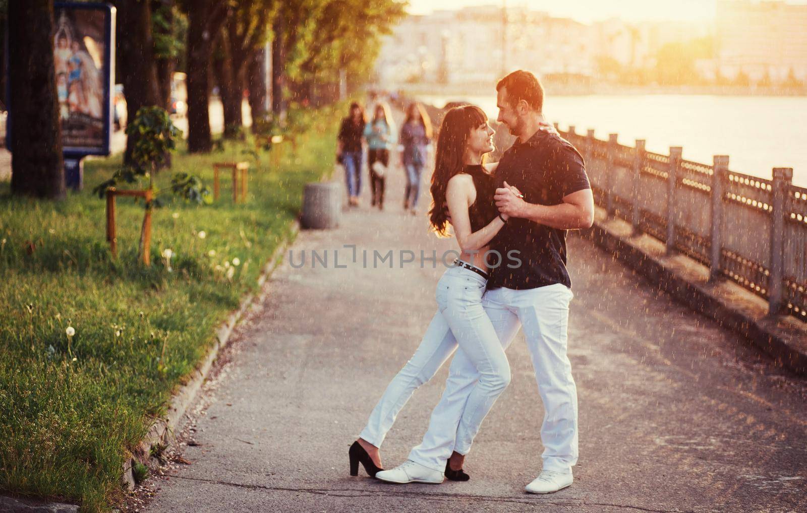 young couple dancing tango on the embankment of the river at sunset