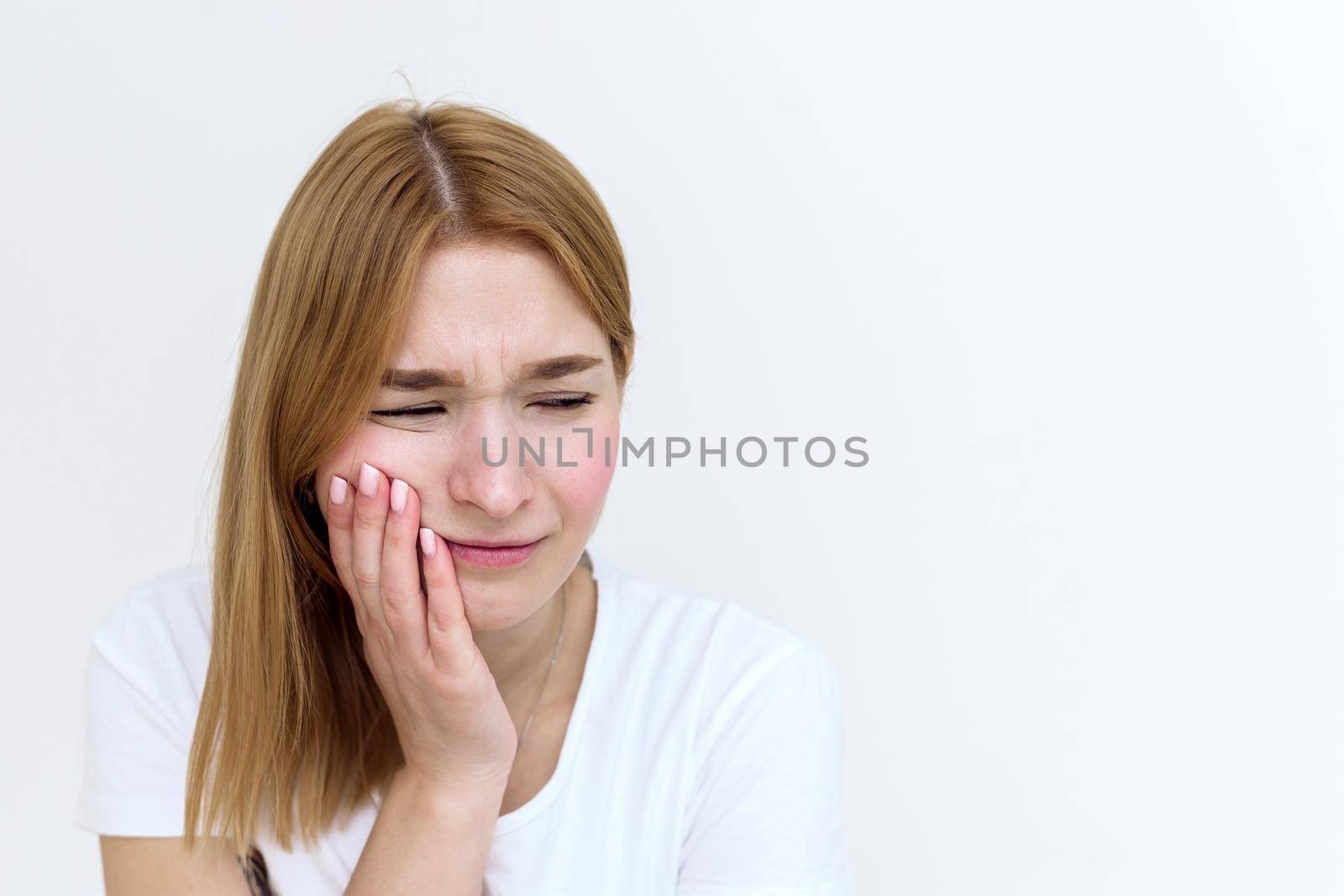 Close-up of a young woman suffering from toothache while sitting in bed. Close-up photo of a man touching her cheek and twisting her lips due to tooth pain.
