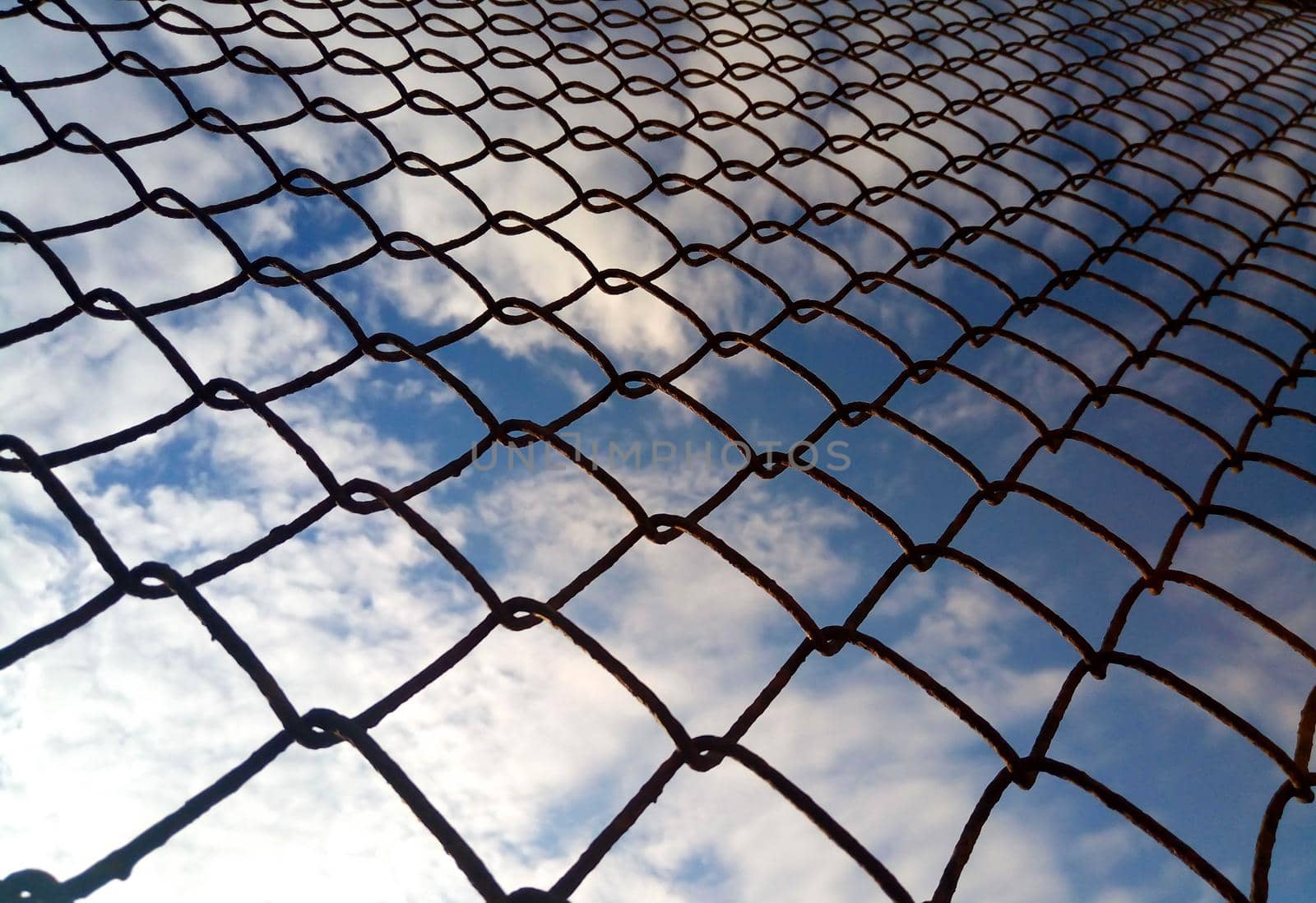 Bright blue sky with white clouds through a metal grid chain fence. Mesh background by lapushka62