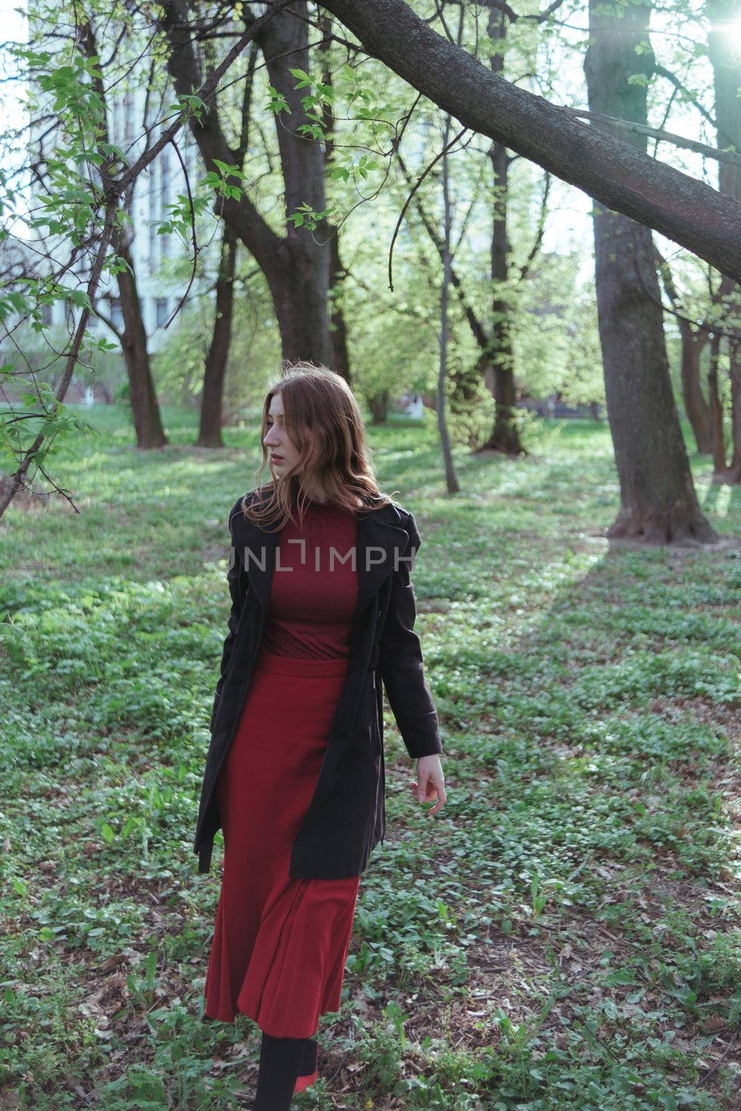 a girl with blonde hair in red golf and a skirt walks through the spring forest by Symonenko