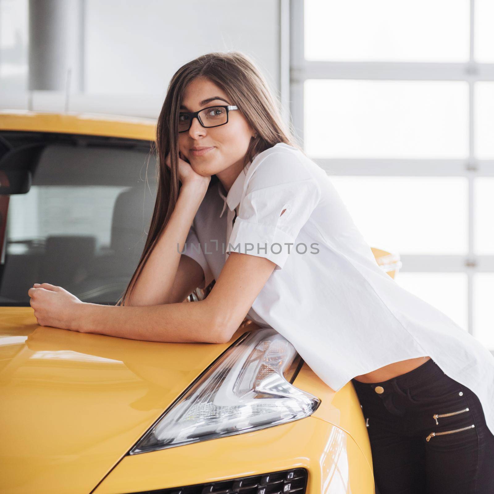 Pretty girl is standing near her car. She is leaning on the roof and is looking aside dreamingly. She is smiling with anticipation