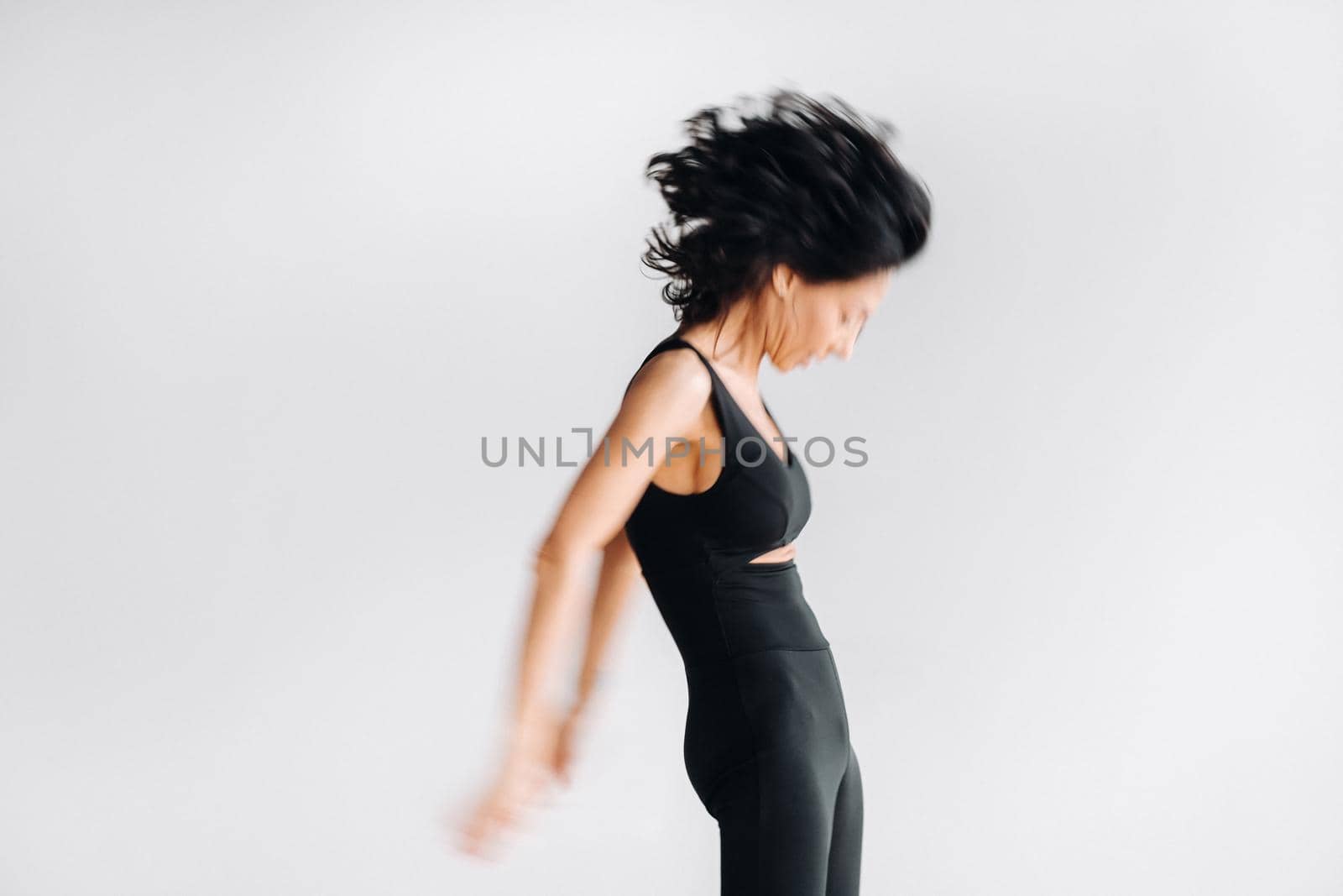 A blurry silhouette of a woman in black sportswear is engaged in dynamic kali meditation in the yoga hall.