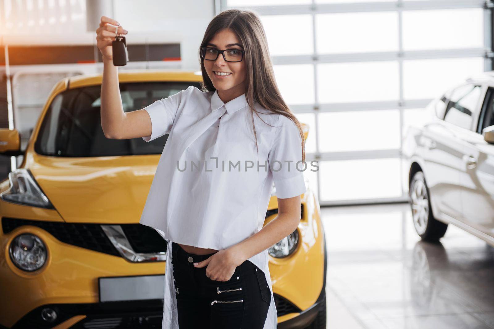 Portrait of a young beautiful woman looking at the camera at the car showing keys.