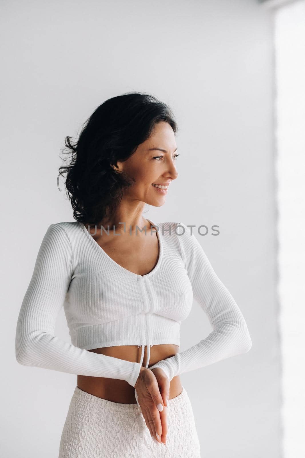 a female yogi in white clothes stands with her hands clasped at the bottom meditating in the yoga hall.