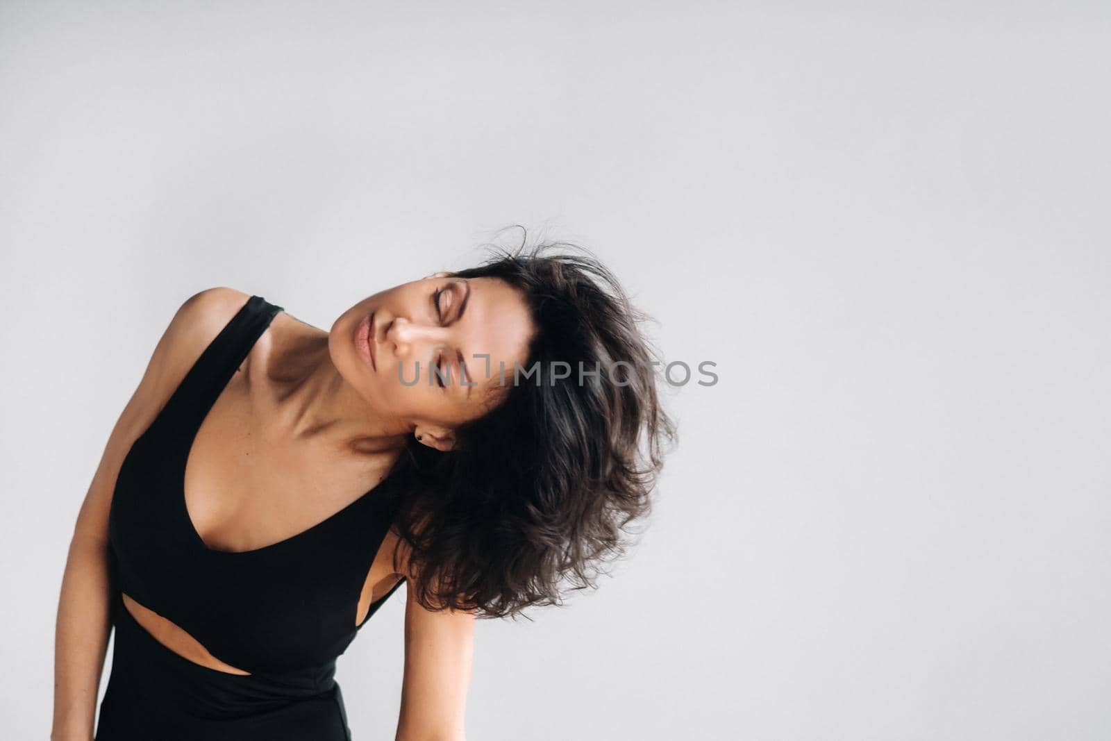 A woman in a black sports T-shirt waves her head with her long hair loose on a gray background.