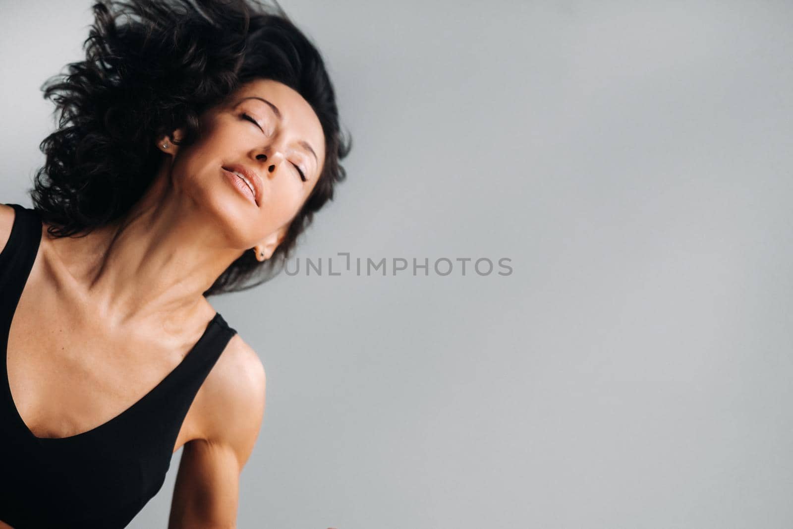 A woman in a black sports T-shirt waves her head with her long hair loose on a gray background.