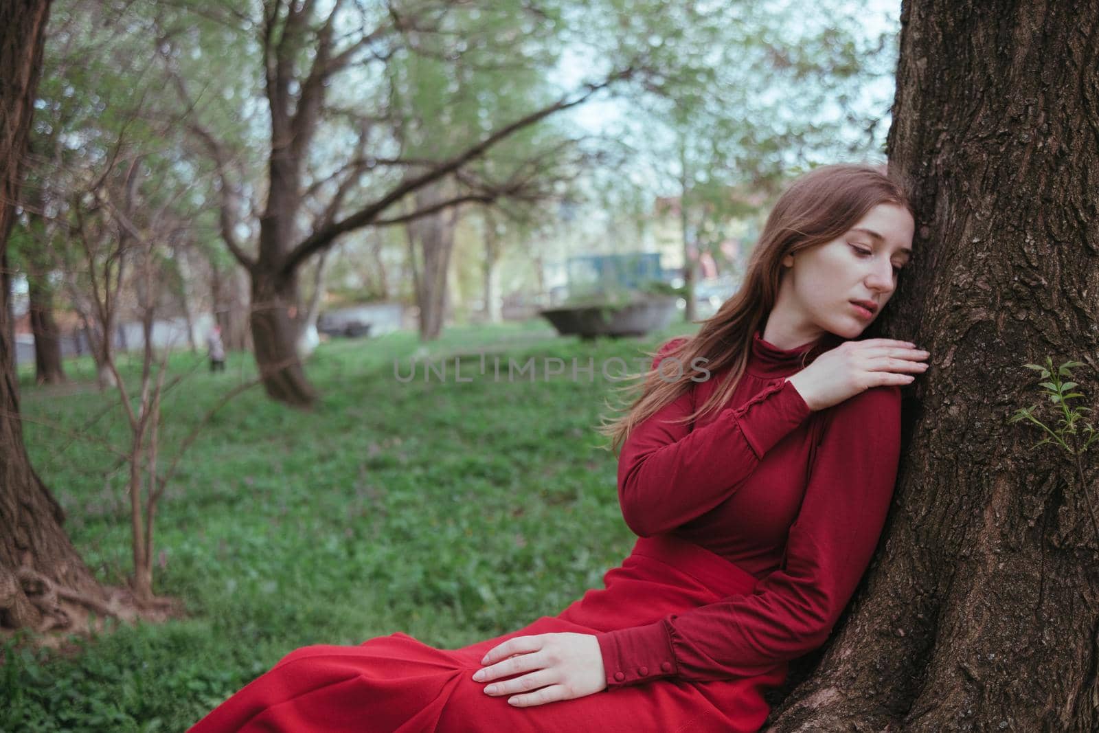a girl in red rests leaning on a tree in the spring forest by Symonenko