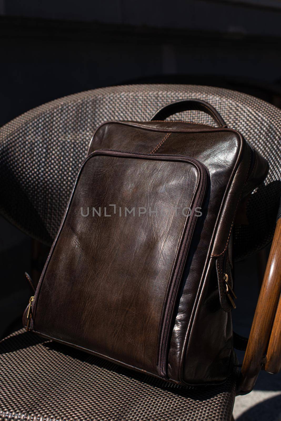Brown leather backpack on the stylish chair. Outdoor photo