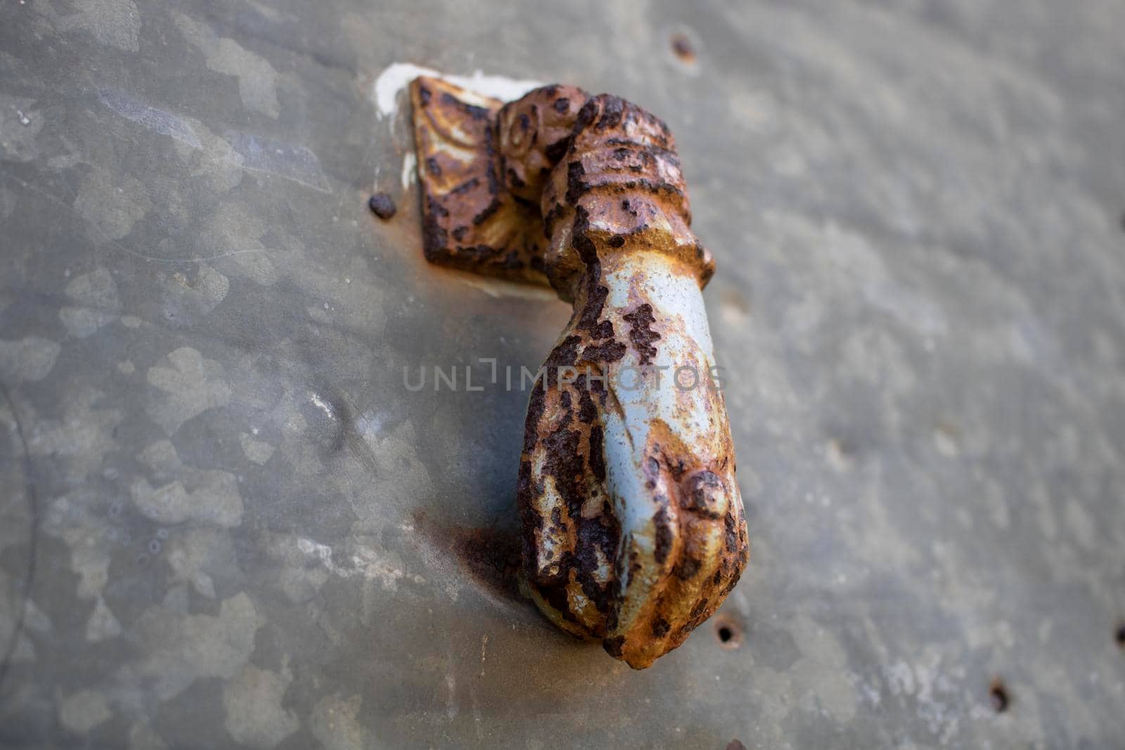 Old classic and rusty door knocker composed by a human hand hanging a ball