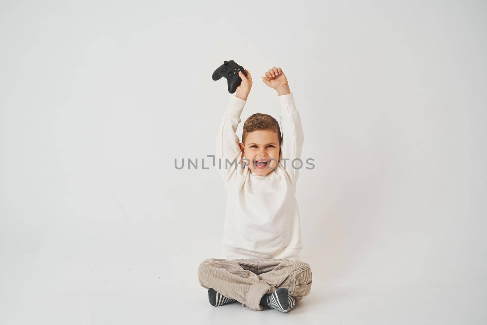 Happy boy with a gamepad raises his hands up and shouts. The emotional child won the console game