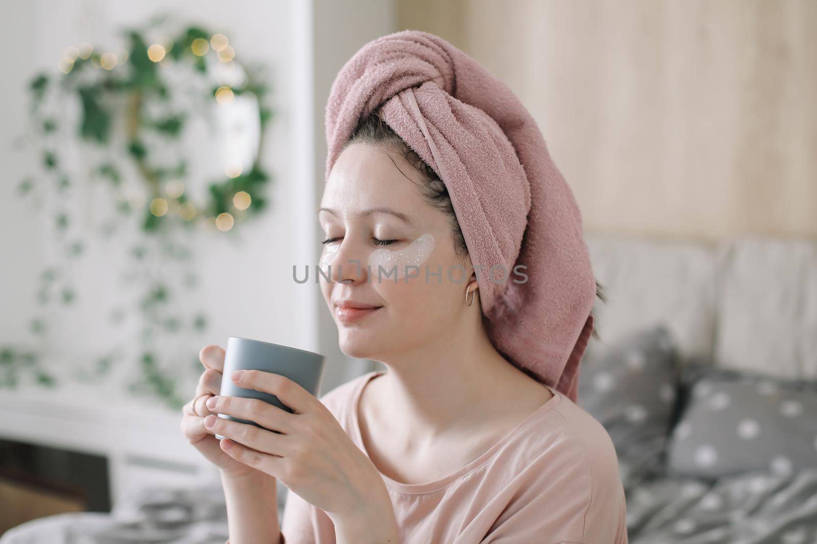 Young woman with eyes patches and towel on head at home. Morning habits and home beauty routine