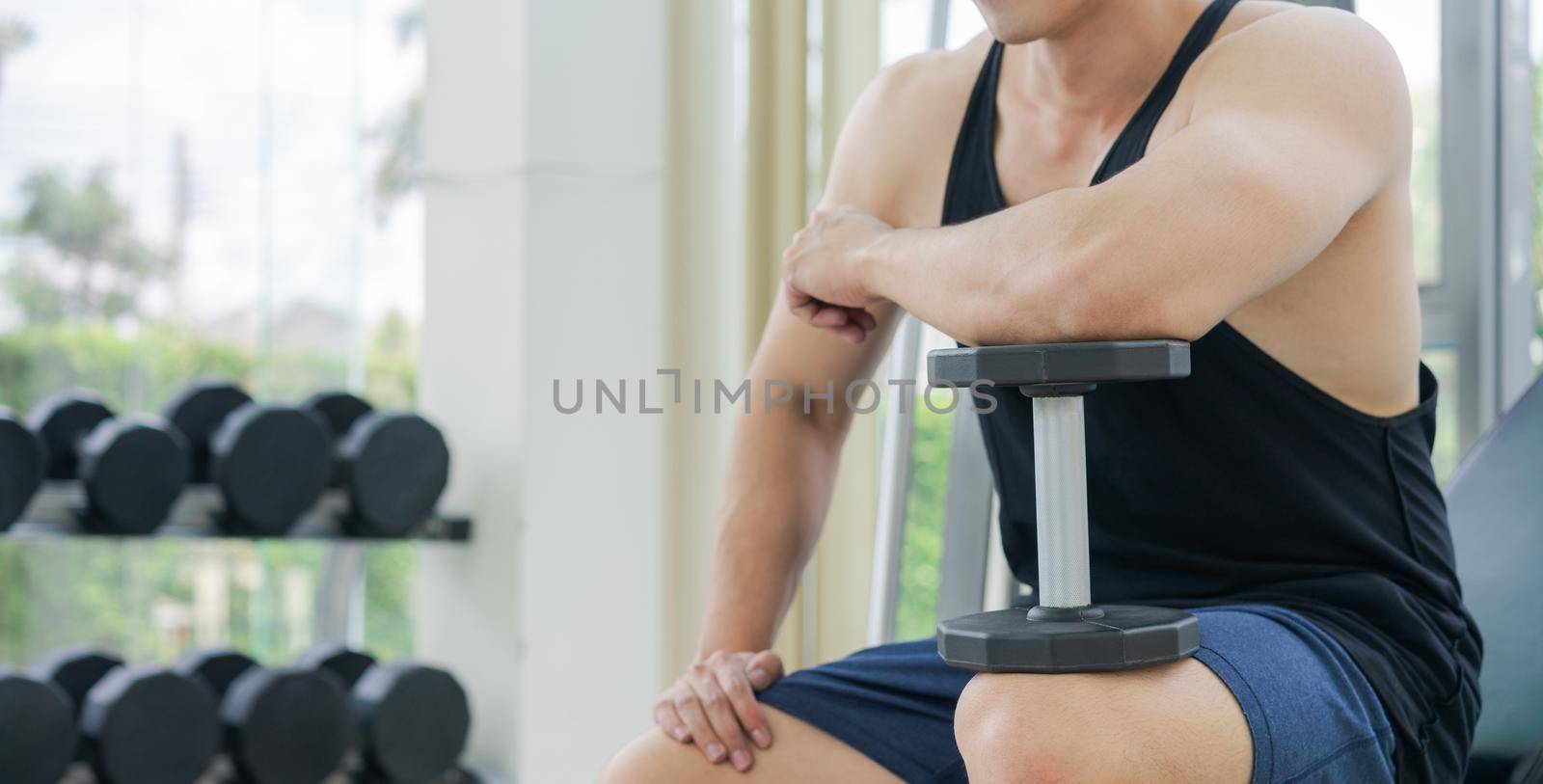 Muscular man bodybuilder in fitness gym training with dumbbells. Healthy lifestyle and bodybuilding concept.