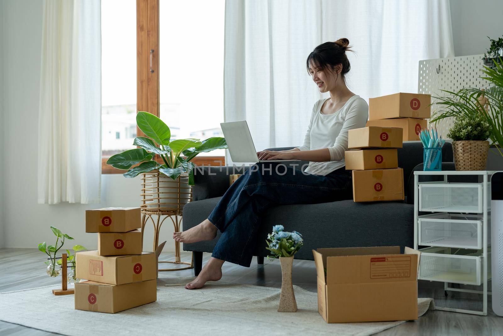 Startup small business owner working with computer at workplace. Freelance woman seller checking orders from laptop. Packing goods for delivery to customer. Online selling. E-commerce.