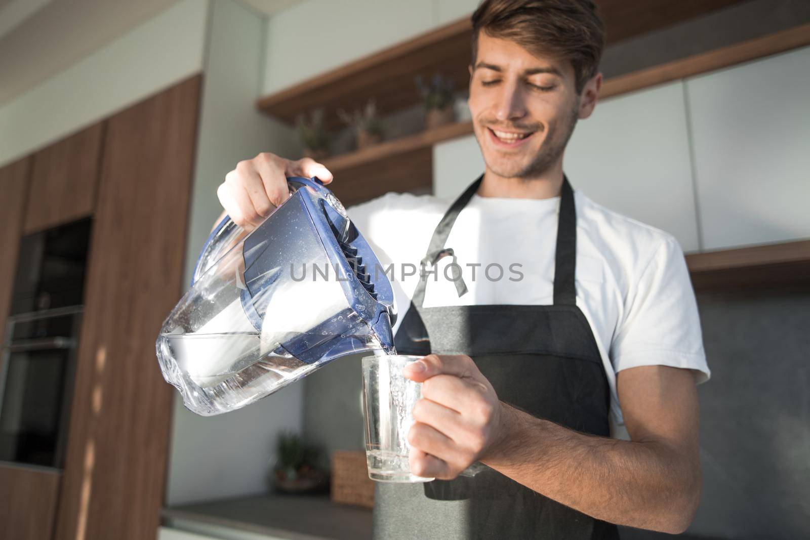 young man pours clean water into a glass by asdf