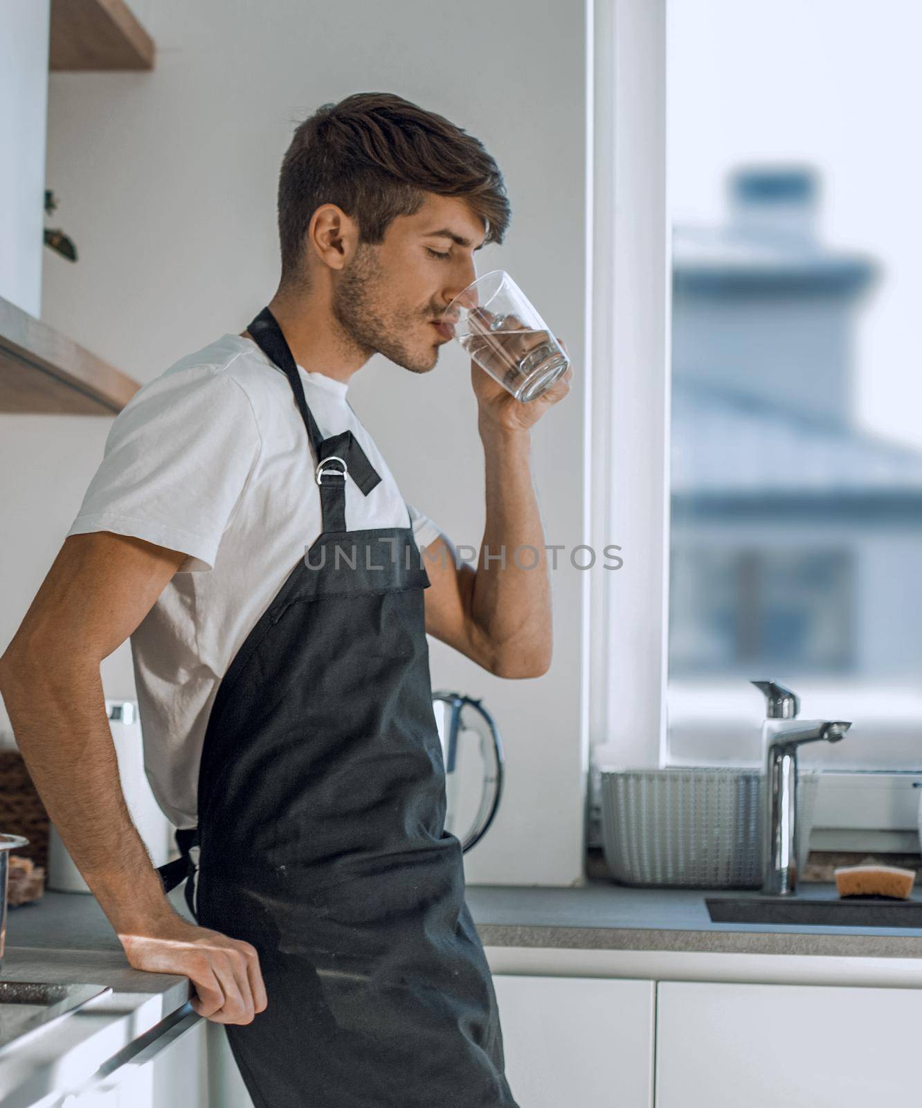 young man drinks clean water standing in the home kitchen. photo with copy space